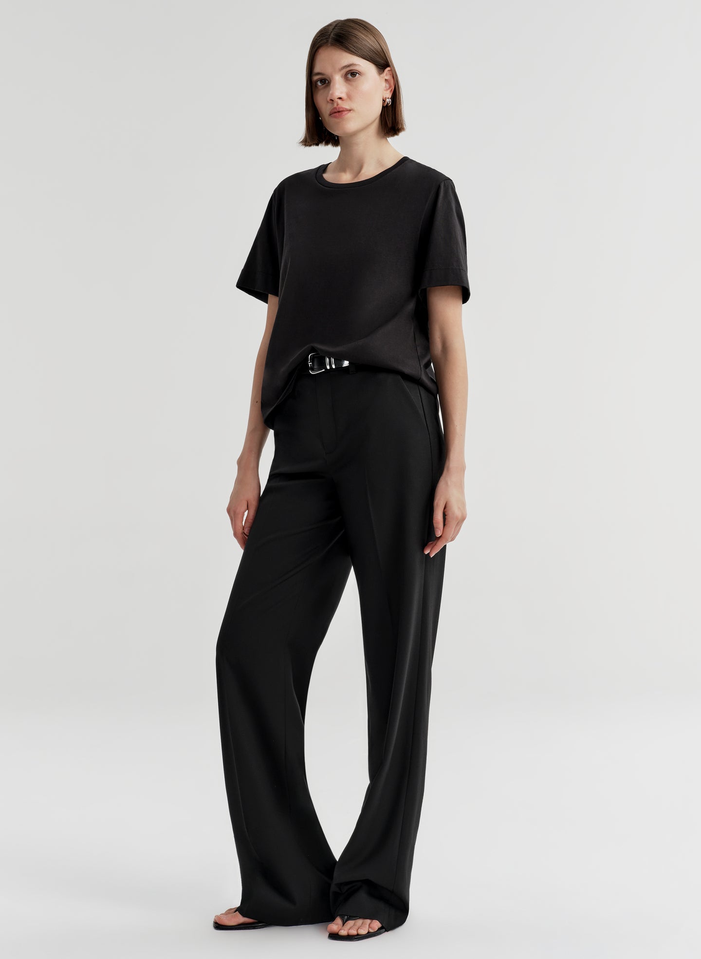 Woman wearing a black t-shirt and black pants on a light gray background