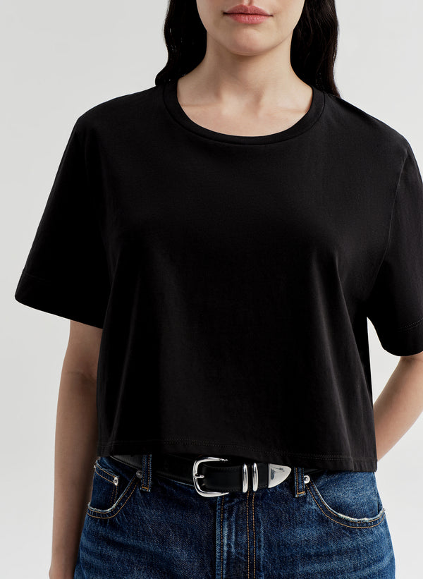 Woman wearing a black t-shirt and blue jeans on a light gray background