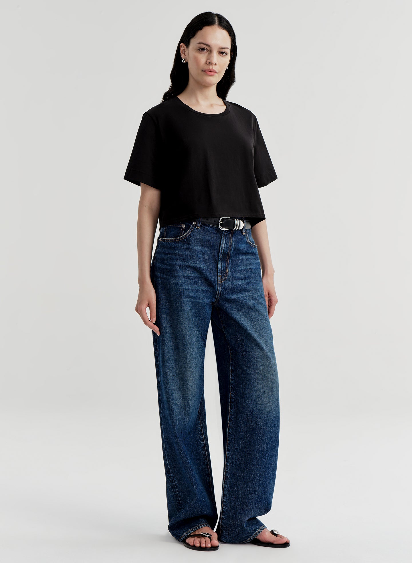 Woman wearing a black t-shirt and blue jeans on a light gray background