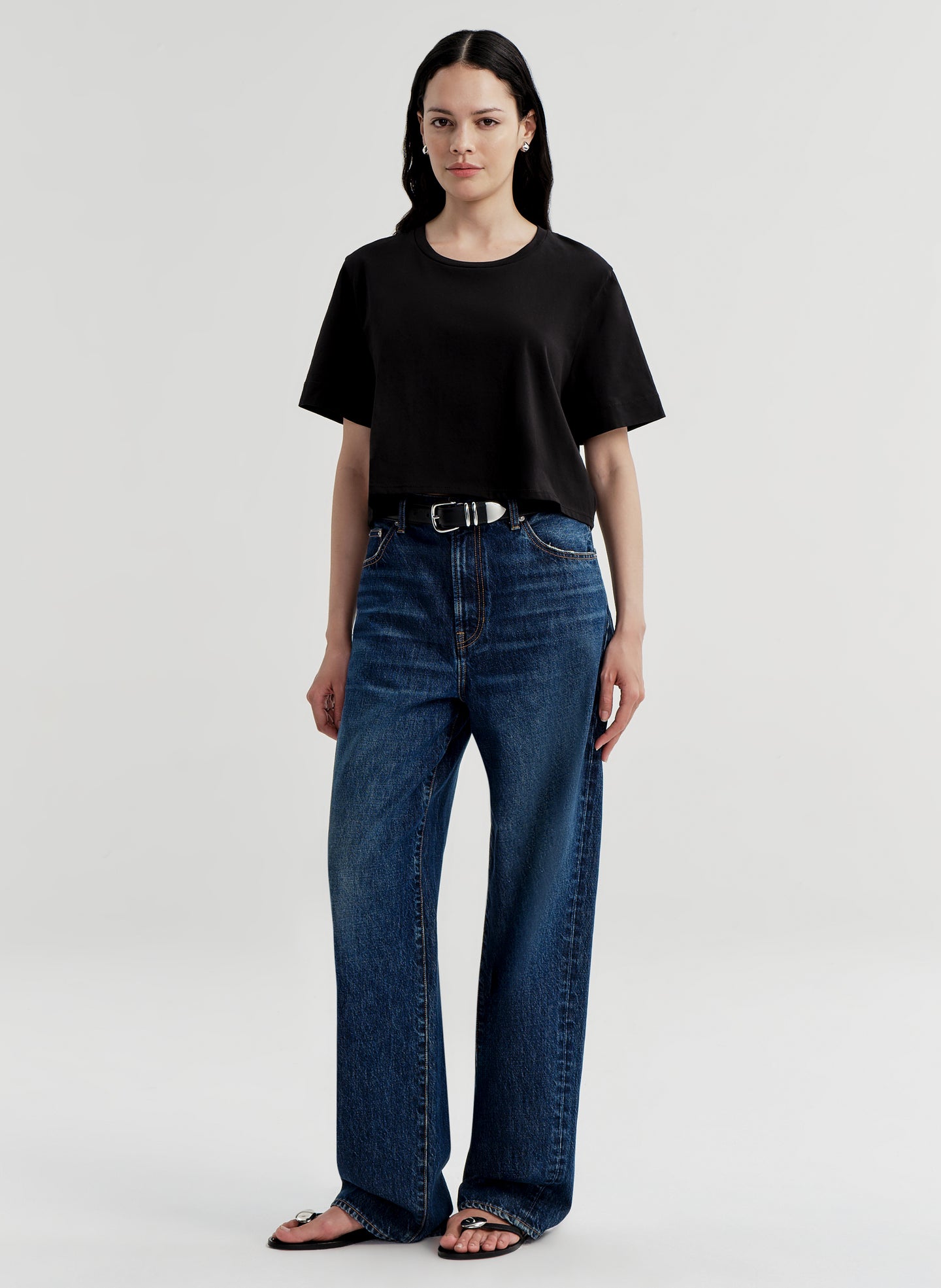 Woman wearing a black t-shirt and blue jeans on a light gray background