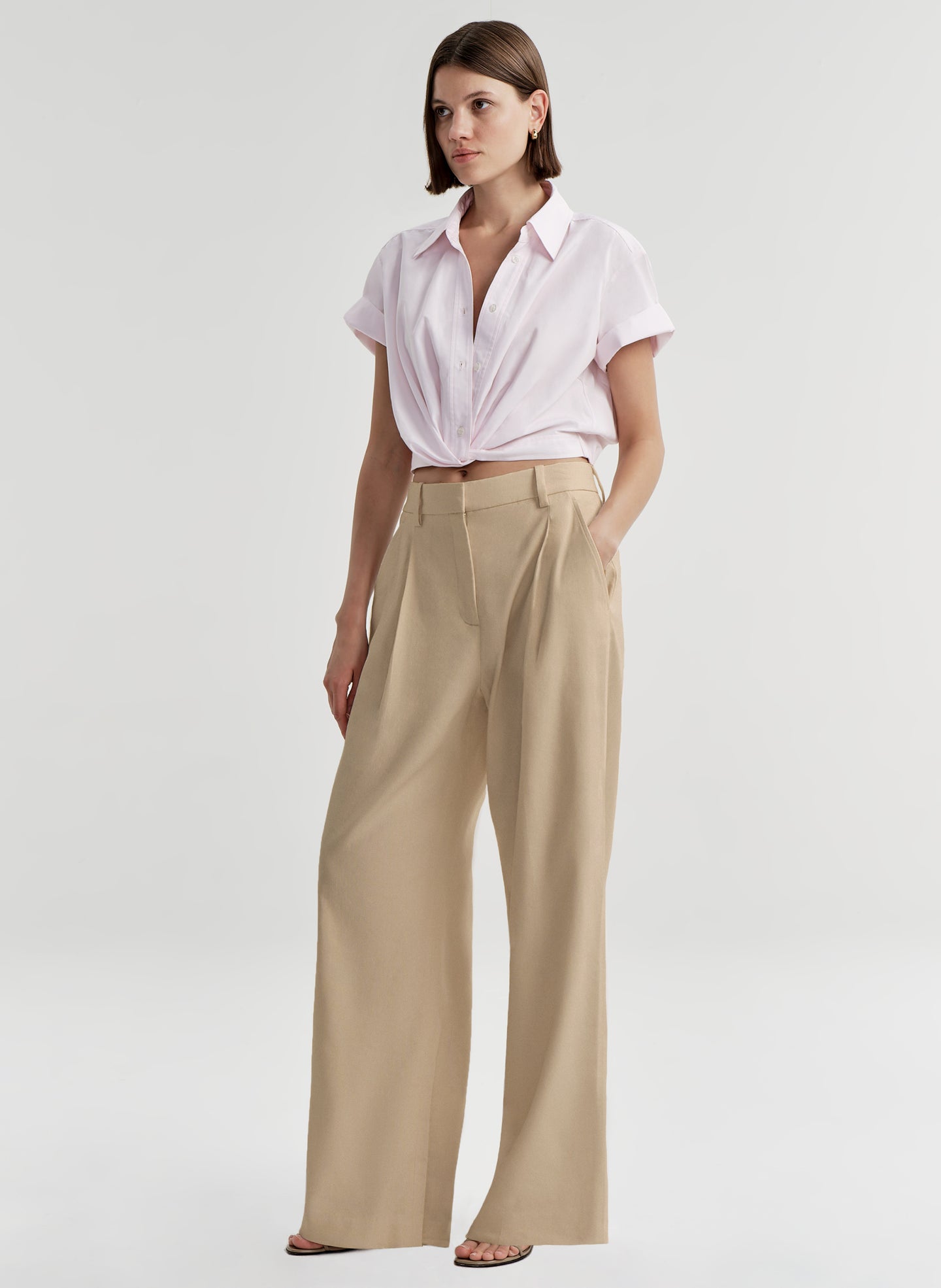 Woman wearing a light pink shirt and beige pants on a light gray background