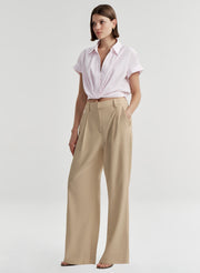 Woman wearing a light pink shirt and beige pants on a light gray background