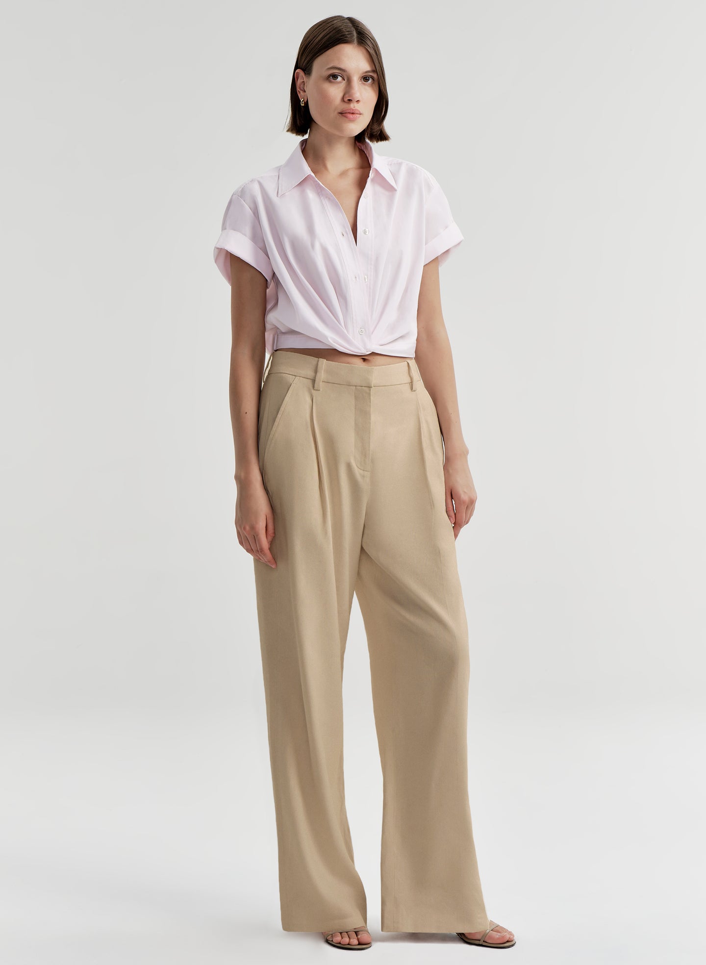 Woman wearing a light pink shirt and beige pants on a light gray background