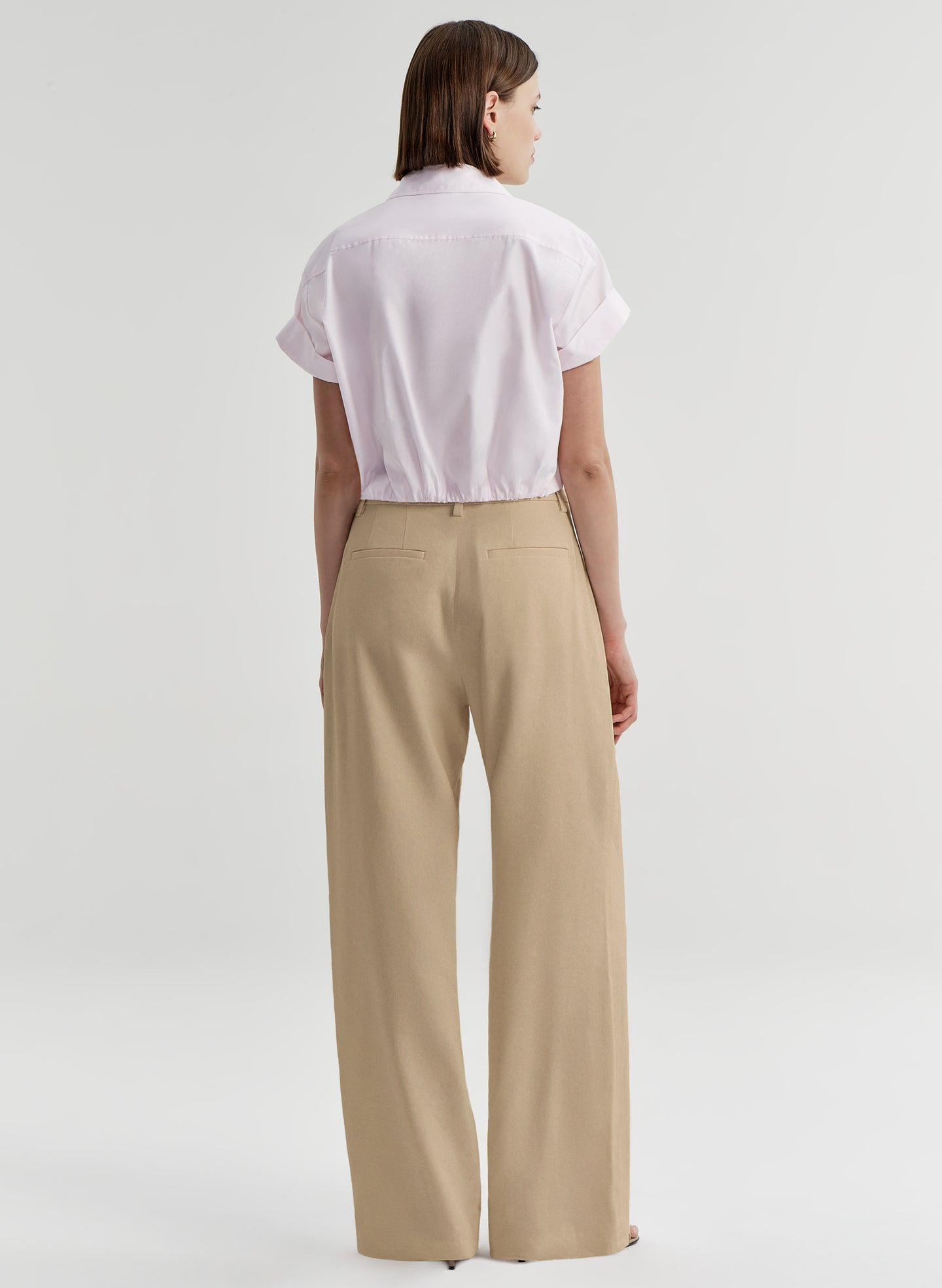 Person wearing a pink shirt and beige pants on a light gray background