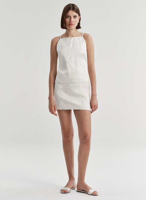 Woman wearing a cream colored mini skirt with a matching top on a plain background 