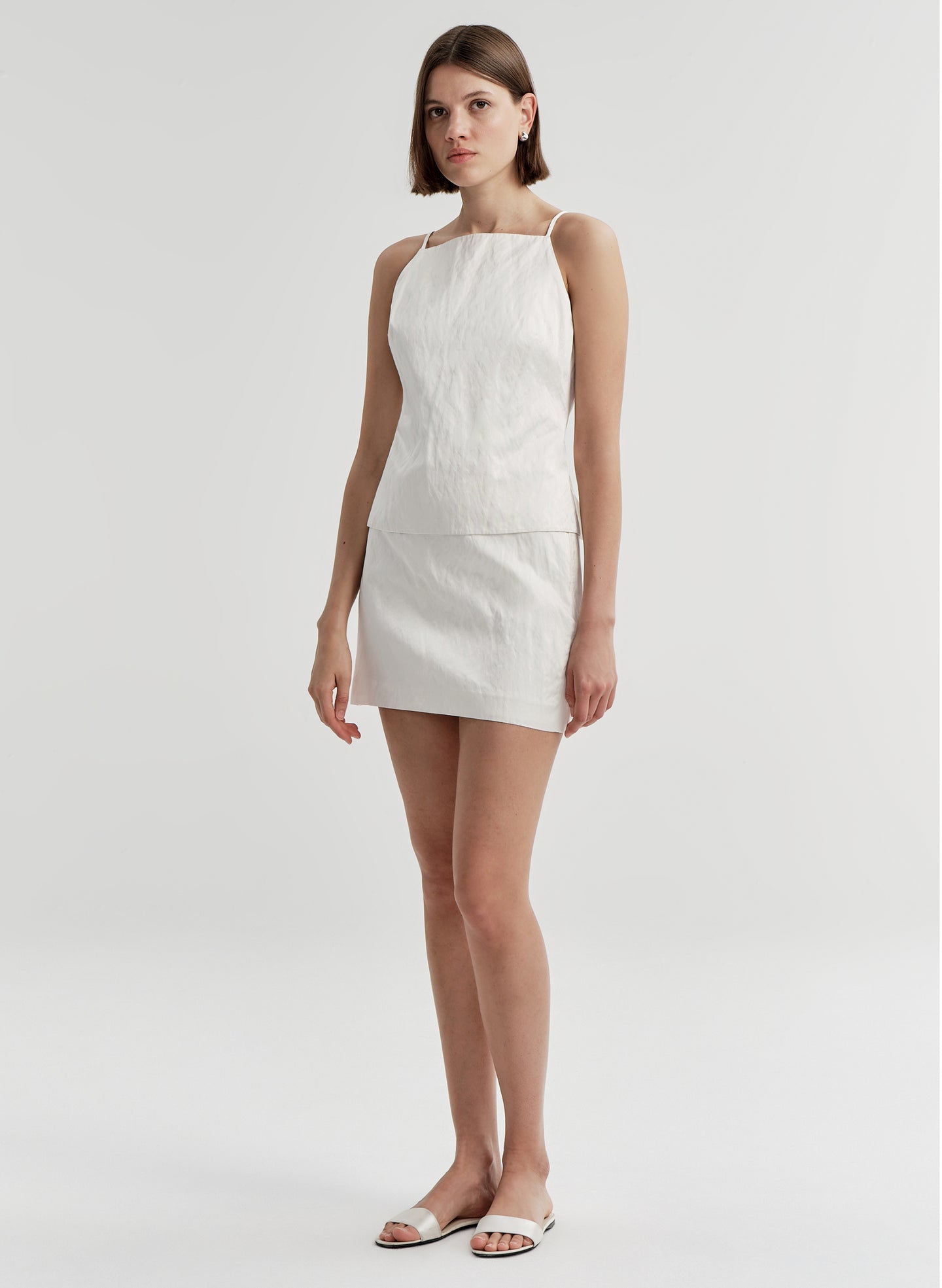 Woman wearing a cream colored mini skirt with a matching top on a plain background 