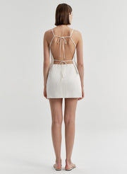 Woman wearing a white open-back top and matching mini skirt on a light gray background