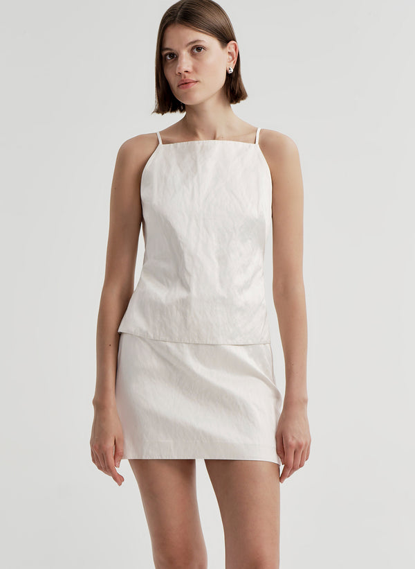Woman wearing a cream sleeveless top against a plain background