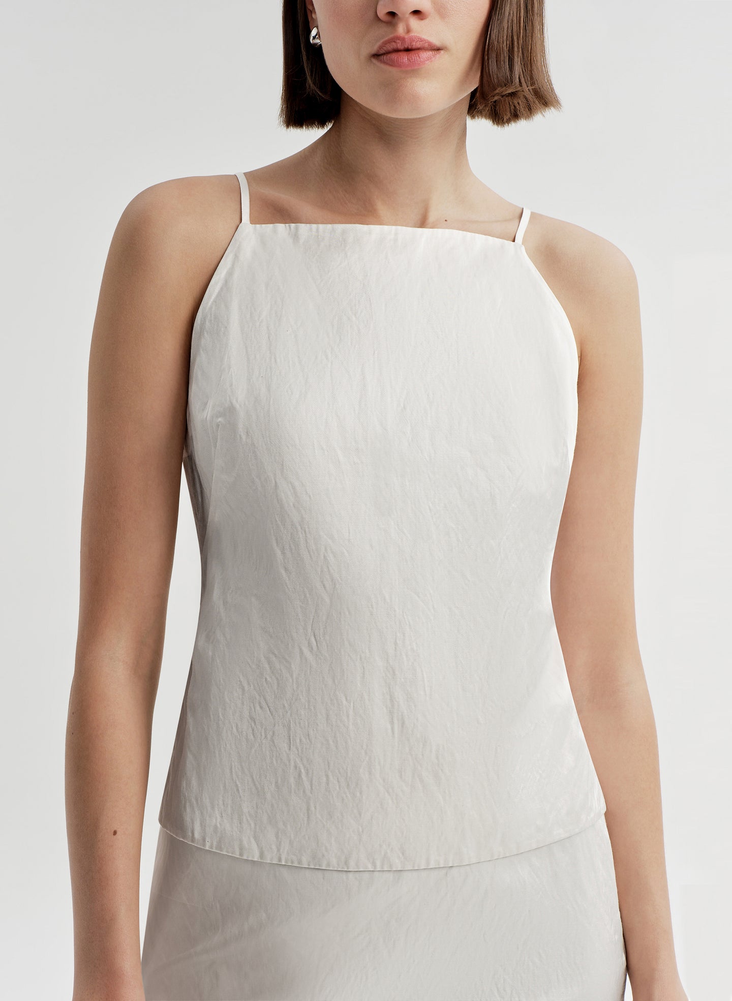 Woman wearing a cream sleeveless top against a plain background
