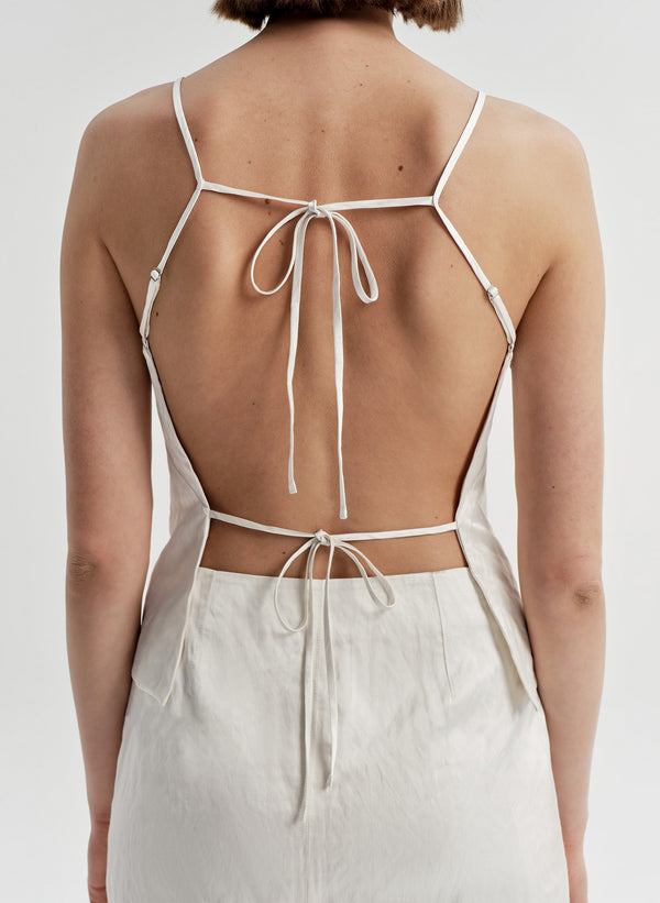 Woman wearing a cream sleeveless top with thin straps and open back on a white background
