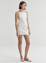 Woman wearing a cream sleeveless top against a plain background