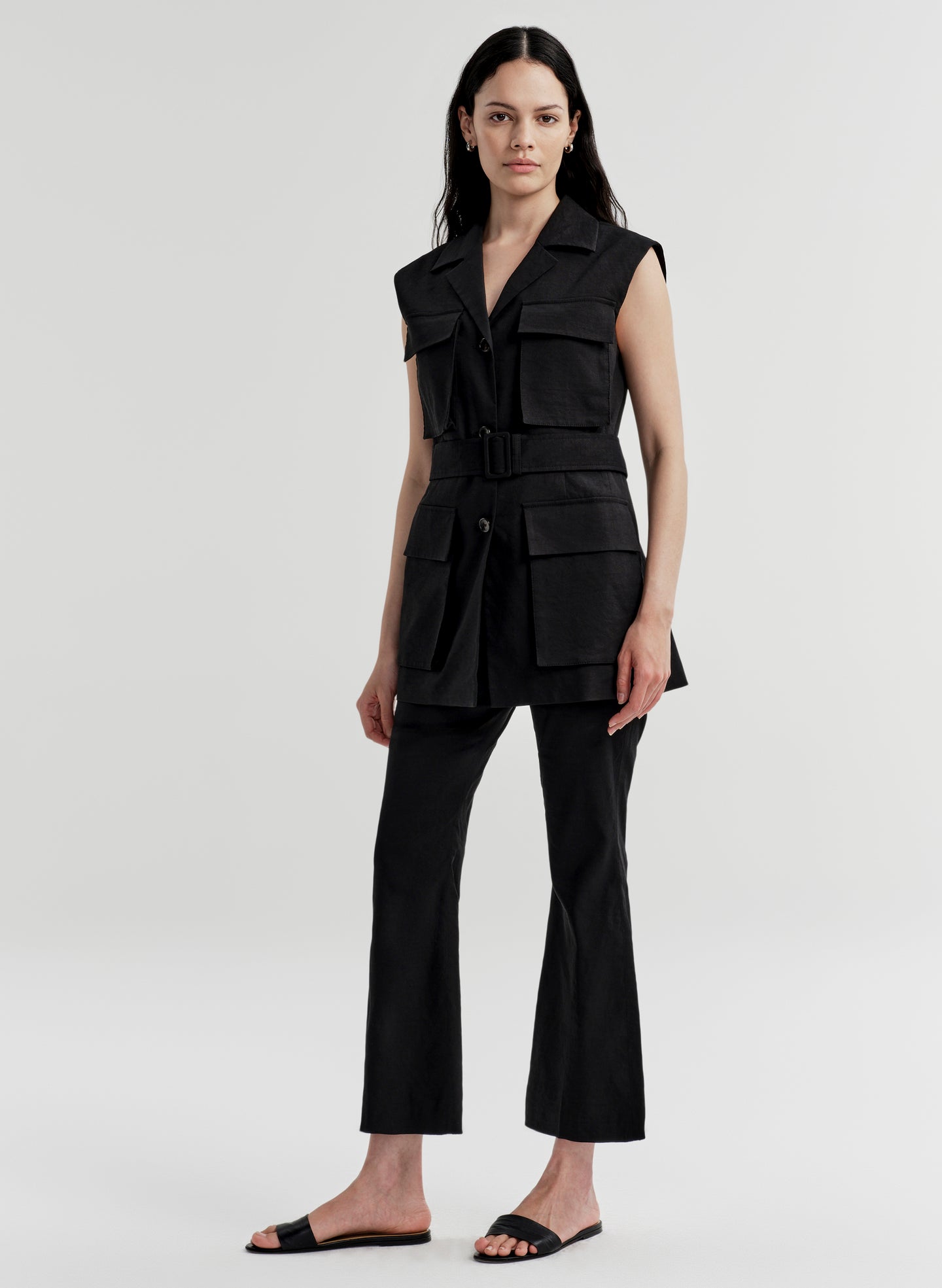 Woman wearing a black sleeveless vest with multiple pockets with black pants on a light gray background