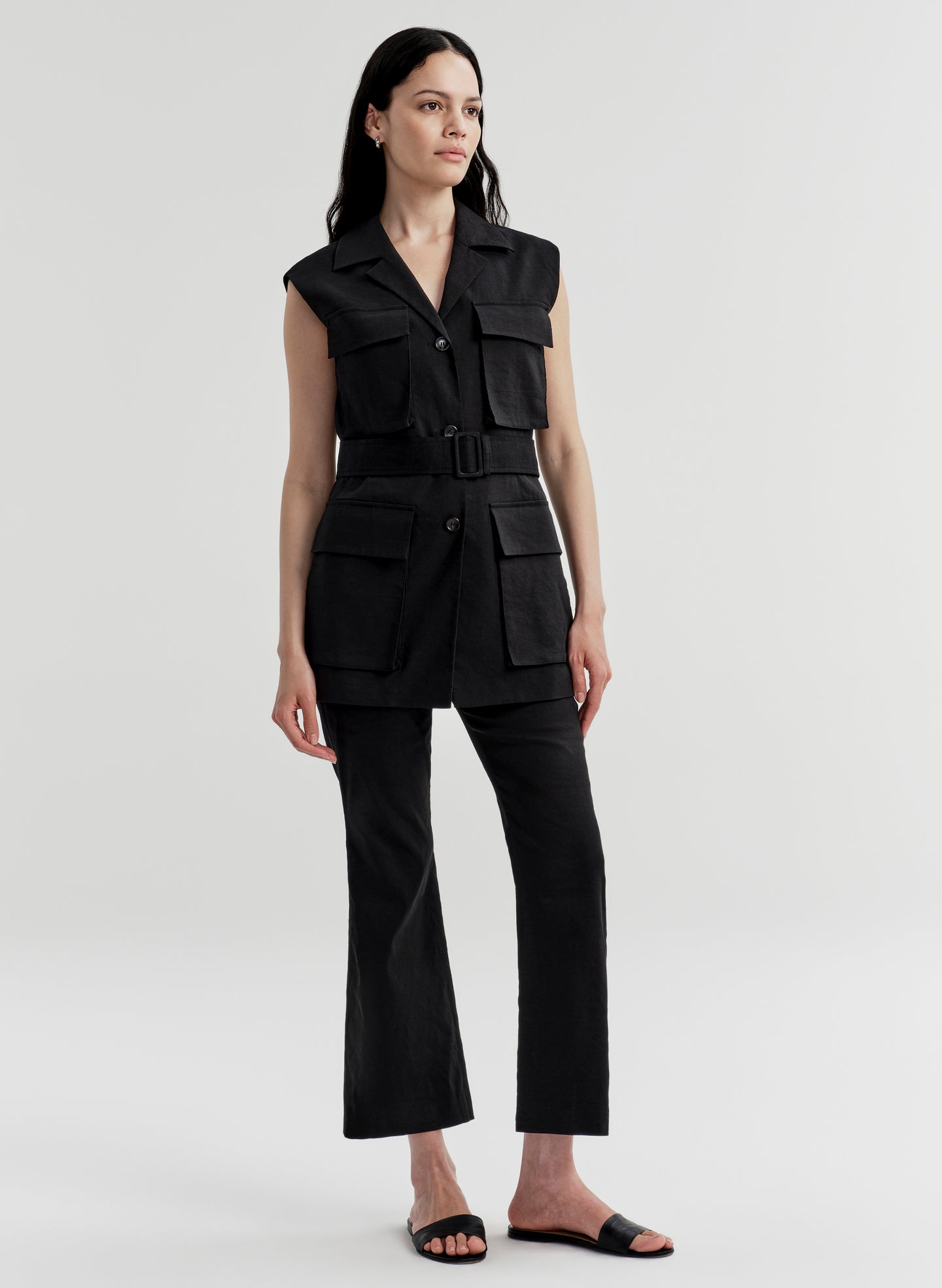 Woman wearing a black sleeveless vest with multiple pockets and black pants on a light gray background