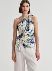 Woman wearing a floral one-shoulder top with white pants on a light gray background