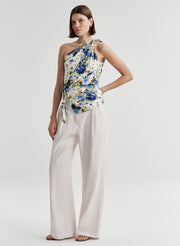Woman wearing a floral one-shoulder top and white pants on a plain background