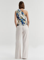 Woman wearing a floral one-shoulder top and white pants on a light gray background