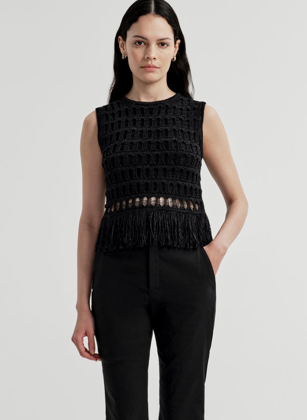 Woman wearing a black sleeveless crochet top with fringe details on a light gray background