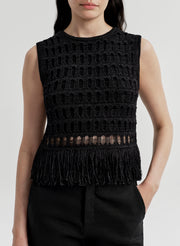 Woman wearing a black sleeveless crochet top with fringe details on a light gray background