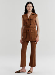 Woman wearing a brown sleeveless vest jacket with a belt and pockets on a white background