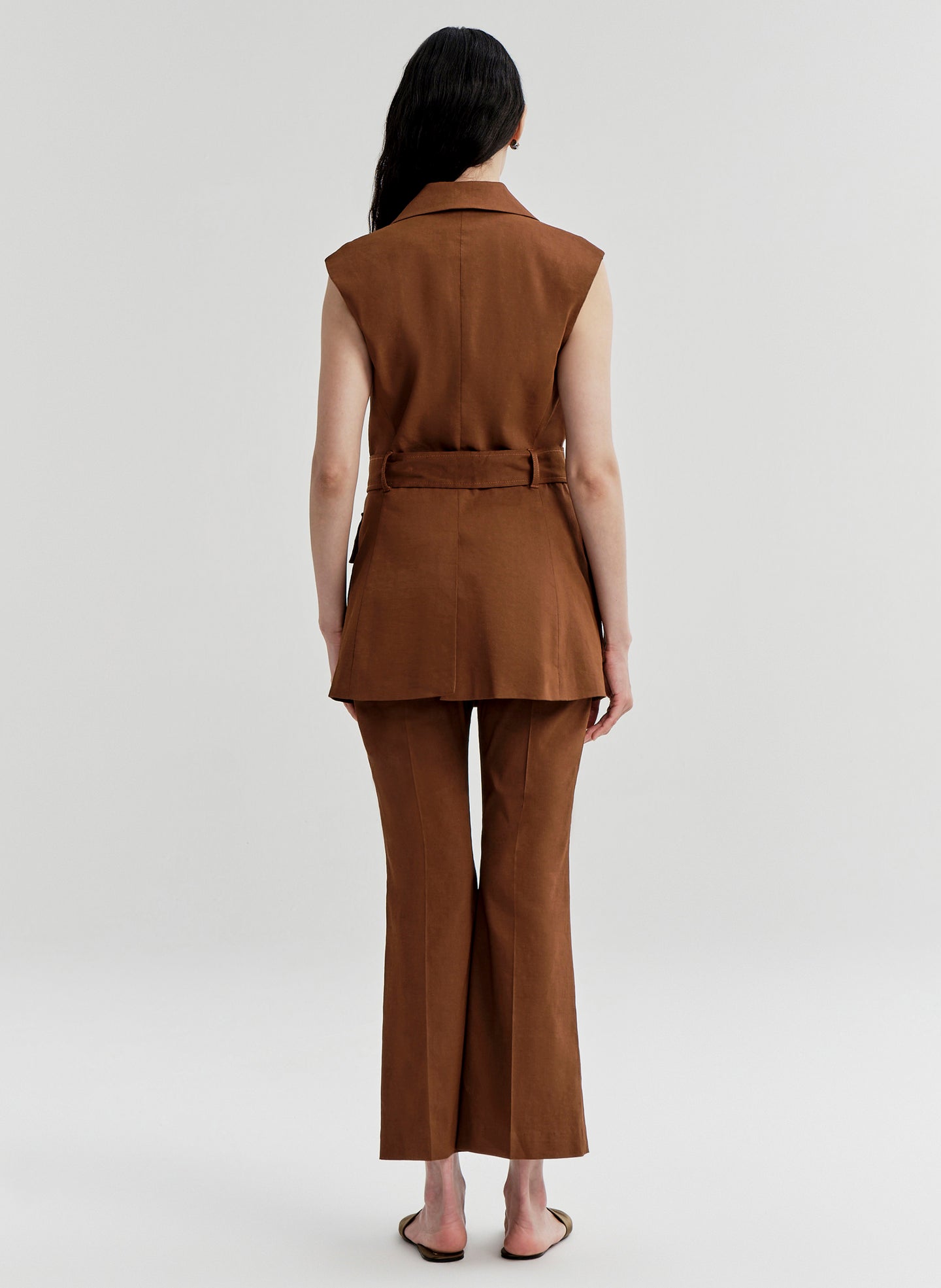 Woman wearing a brown sleeveless jacket and pants set on a white background