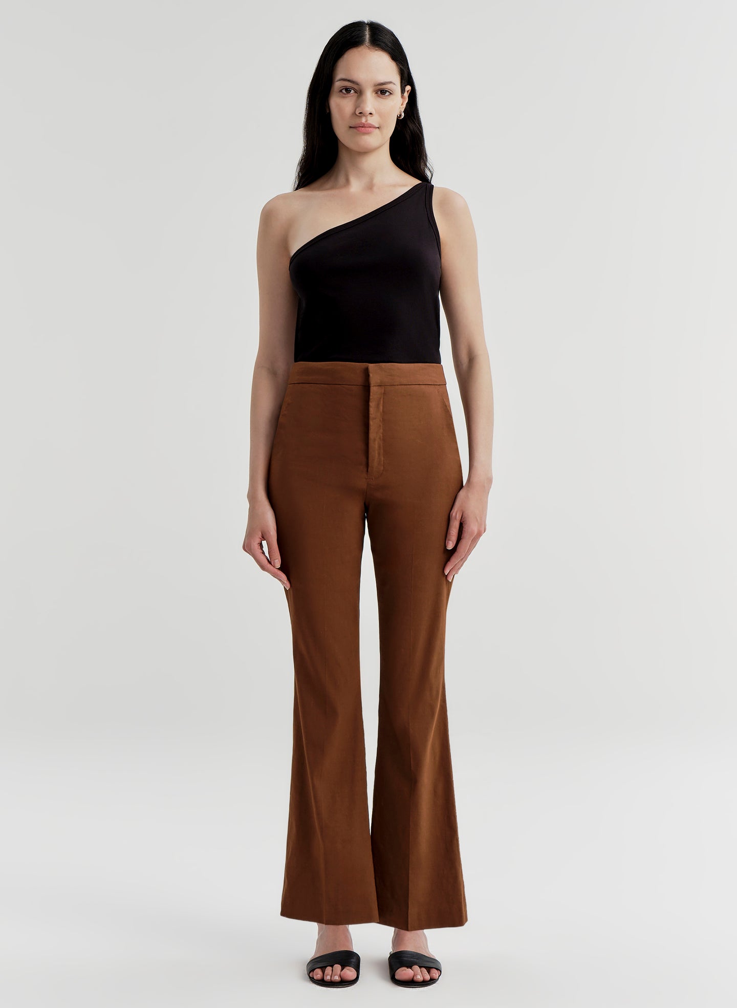 Woman wearing brown linen pants and a black top on a white background