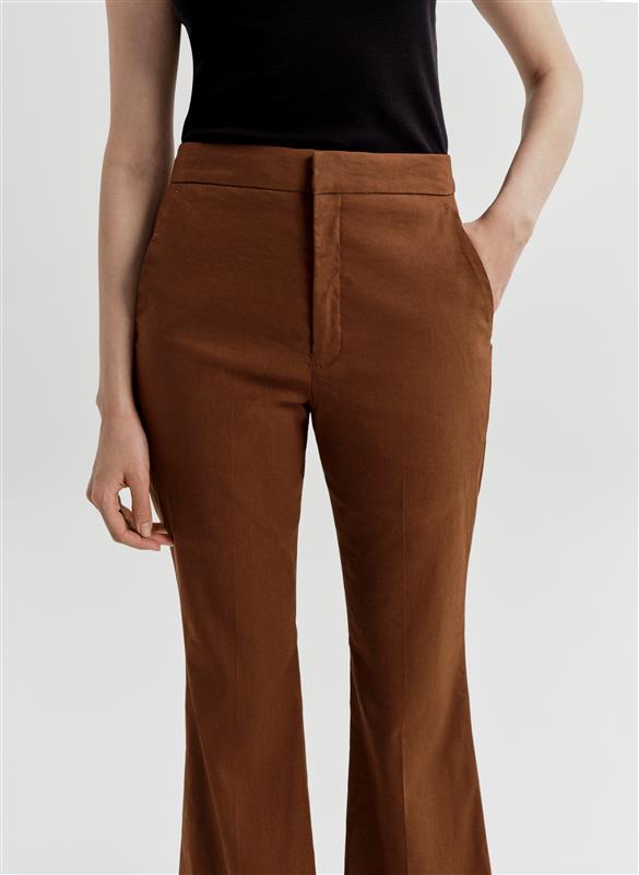 Woman wearing brown linen pants and a black top on a white background
