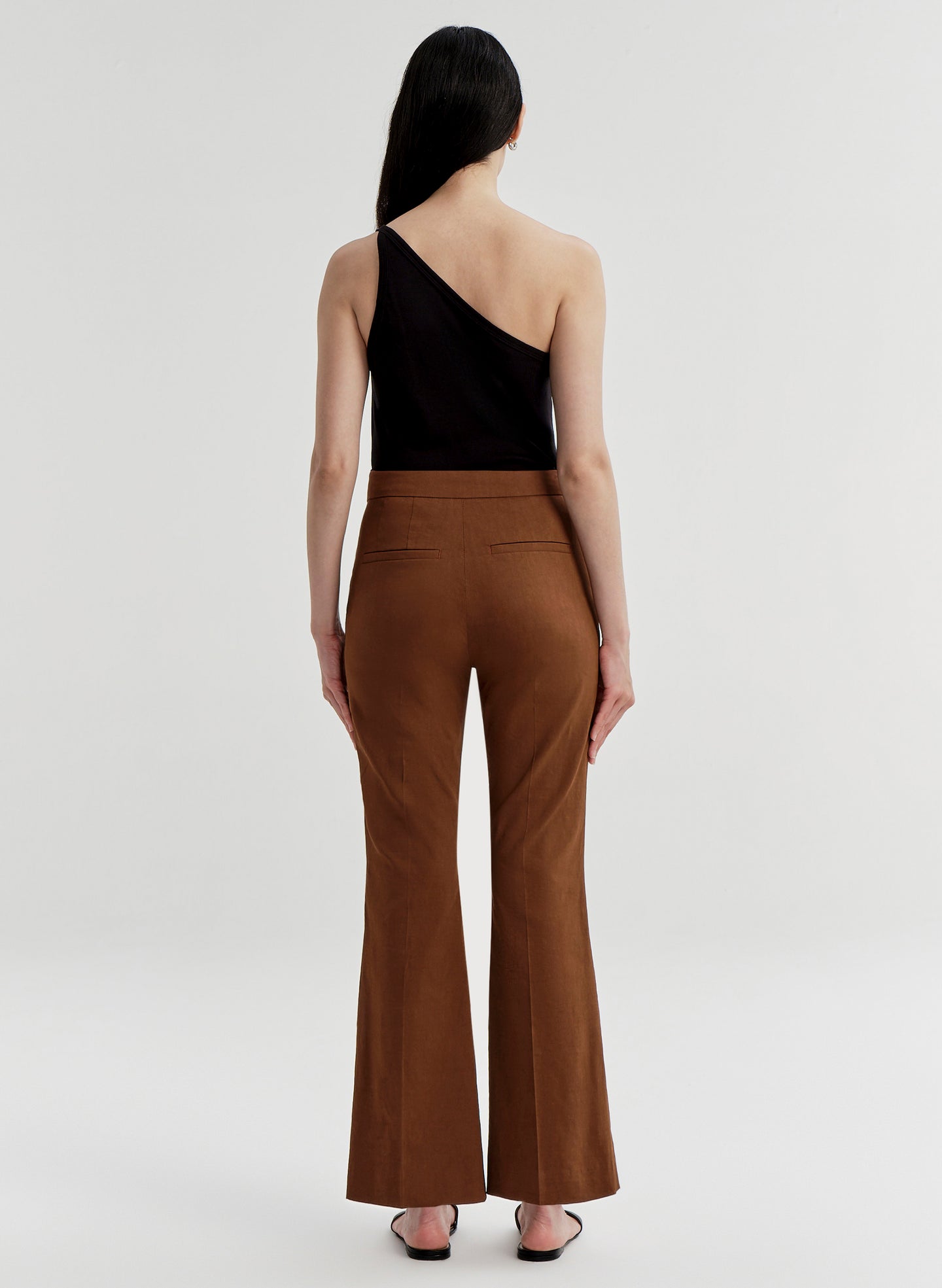 Woman wearing brown linen pants and a black top on a white background