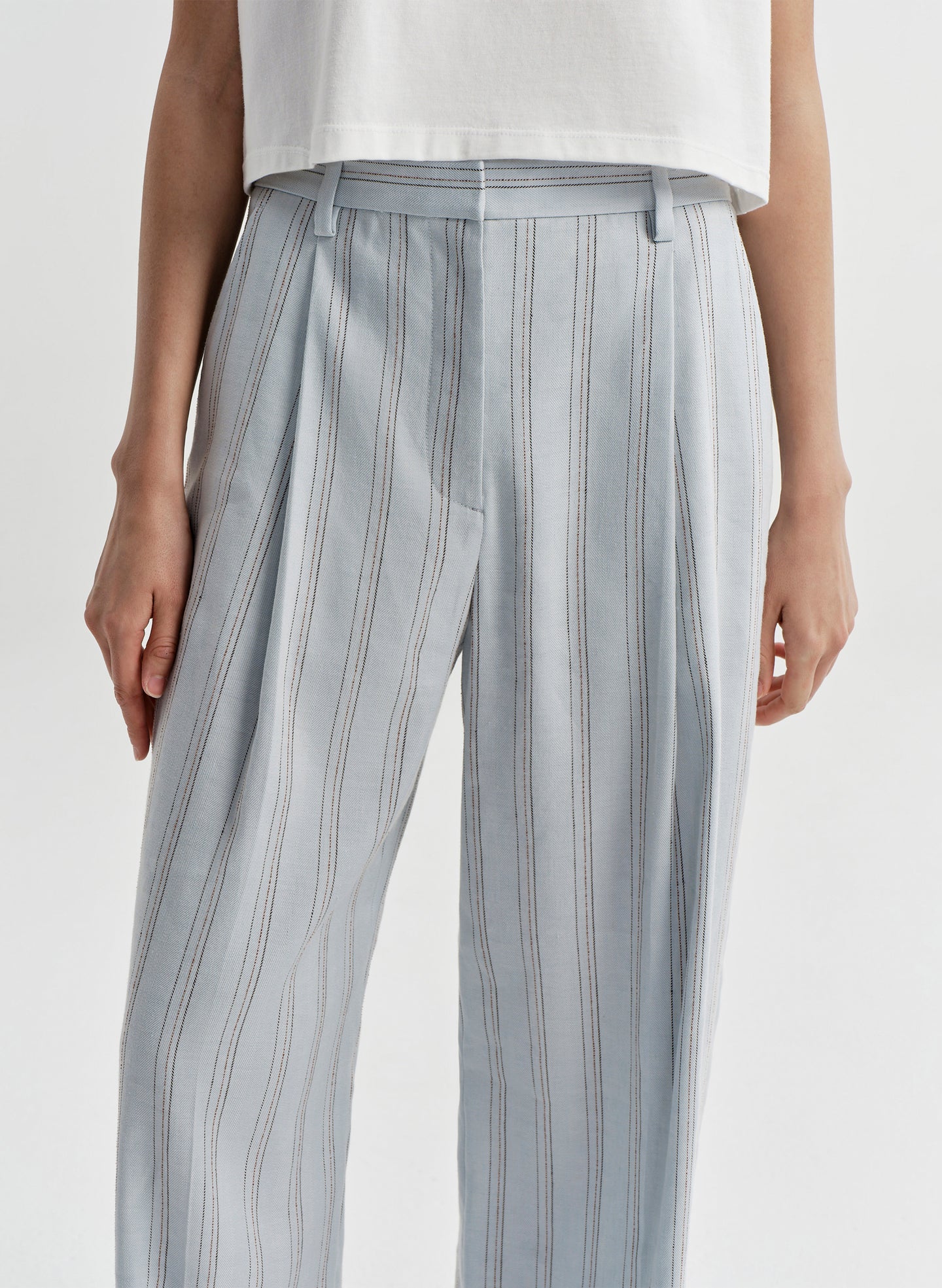 Woman wearing striped linen pants with a white top on a white background