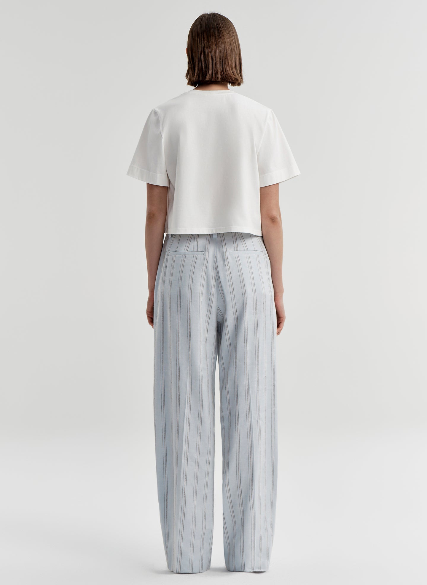 Woman wearing striped linen pants with a white top on a white background