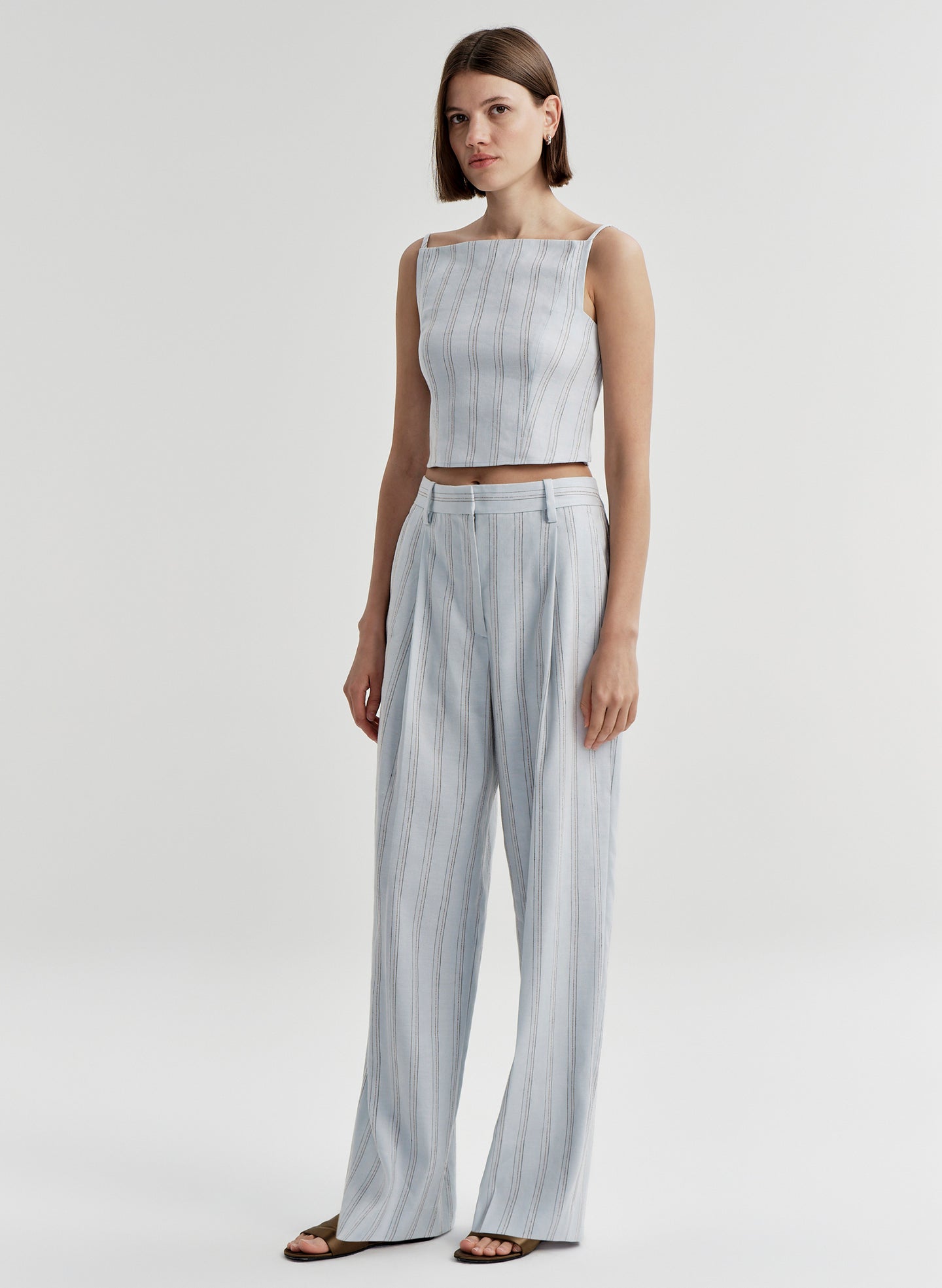 Woman wearing a light blue striped sleeveless top and matching pants on a white background
