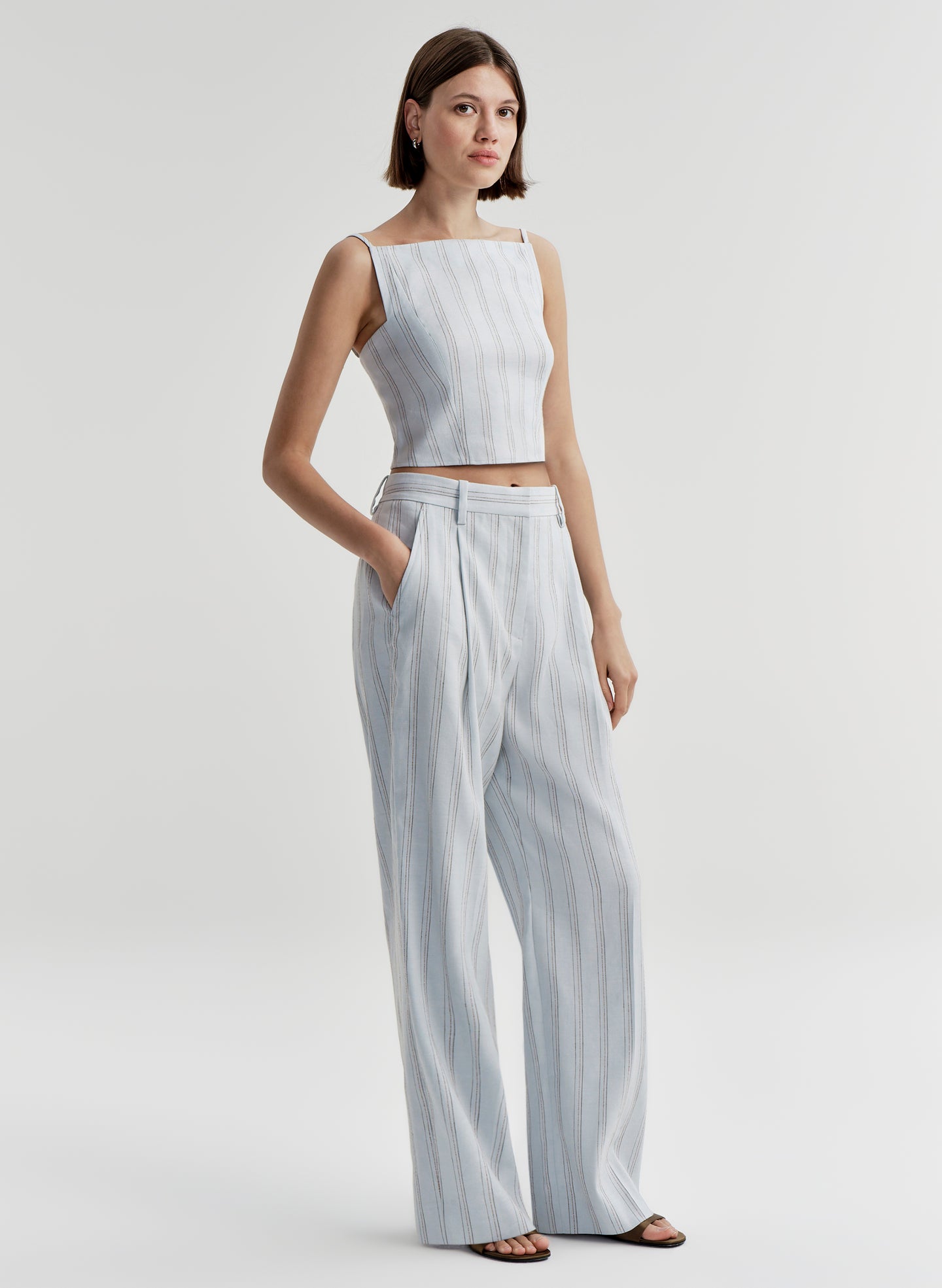 Woman wearing a light blue striped sleeveless top and matching pants on a white background