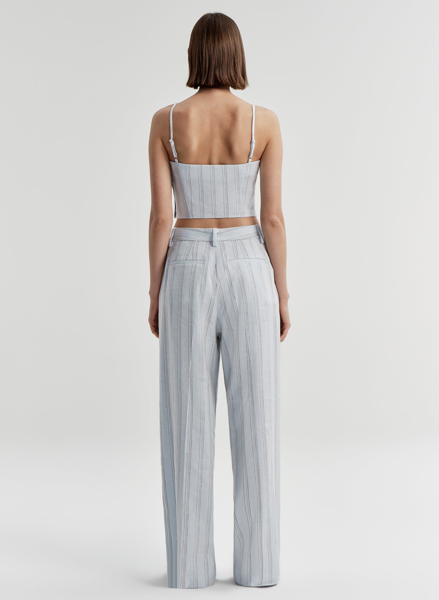 Woman wearing a light blue striped sleeveless top and matching pants on a white background