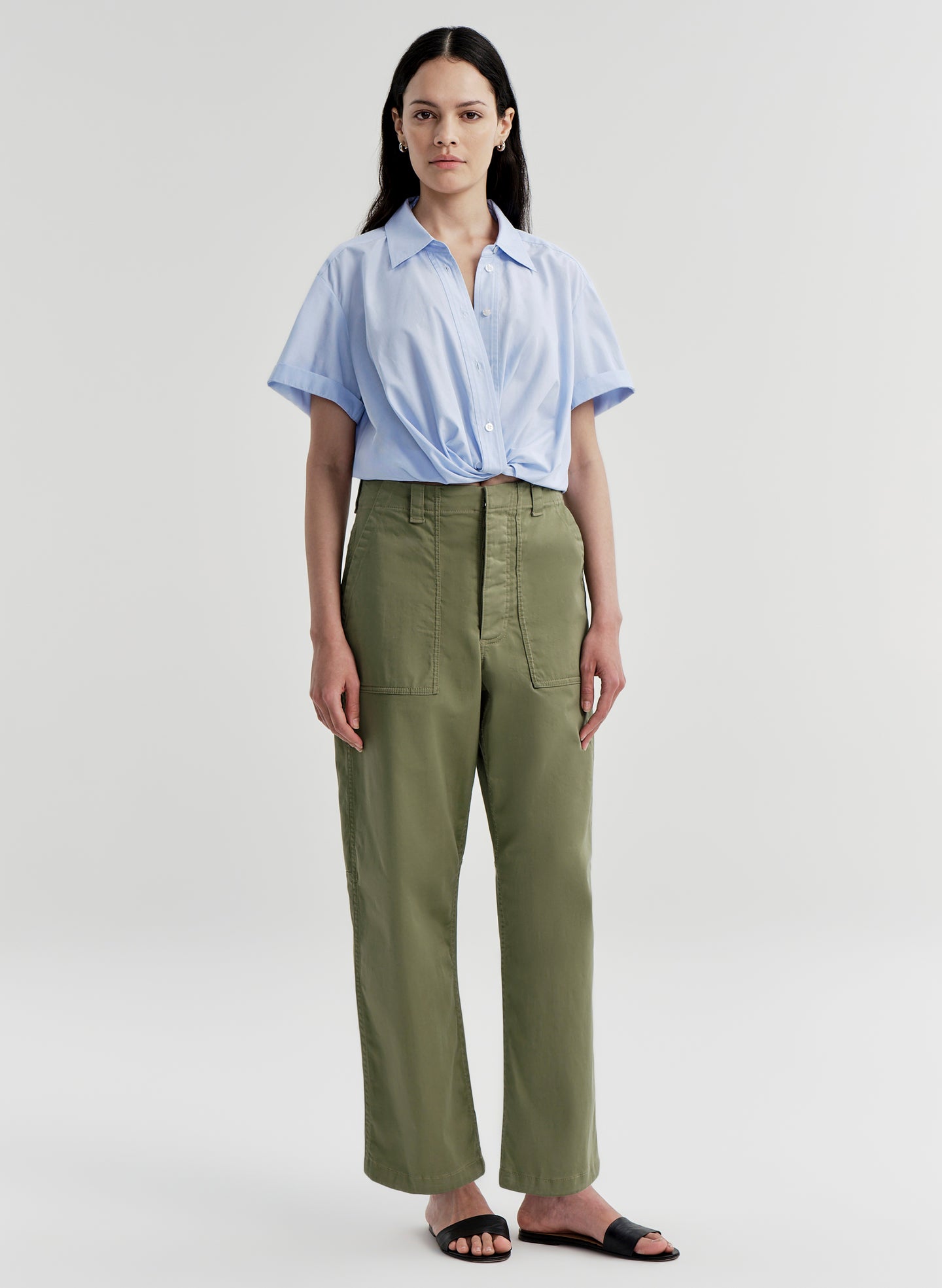 Woman wearing a light blue shirt and green pants on a white background