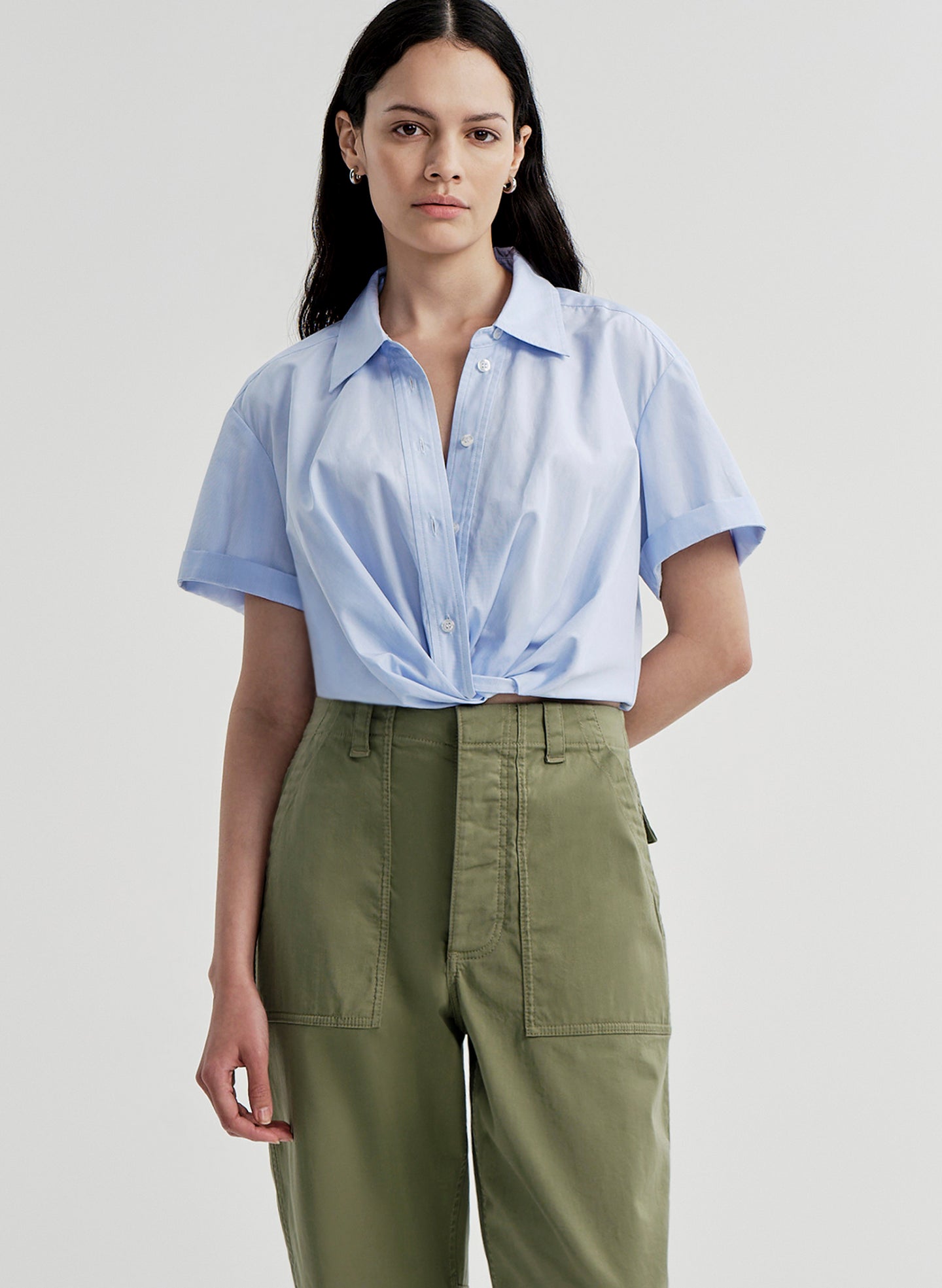 Woman wearing a light blue shirt and green pants on a plain background