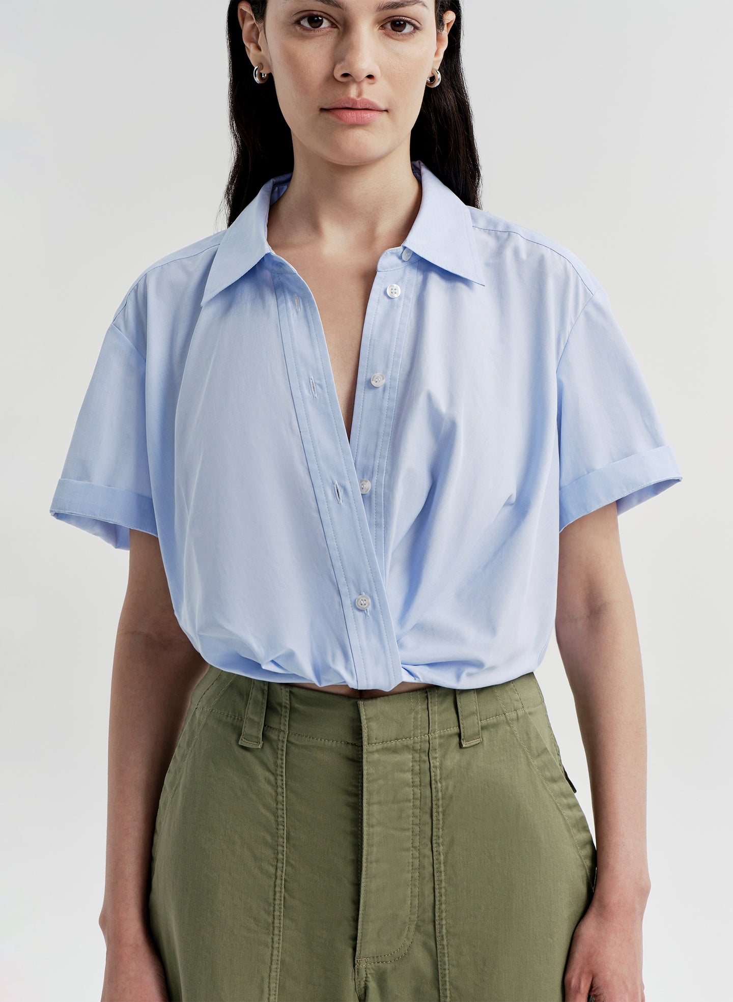 Woman wearing a light blue shirt and green pants on a plain background