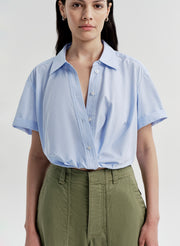 Woman wearing a light blue shirt and green pants on a plain background