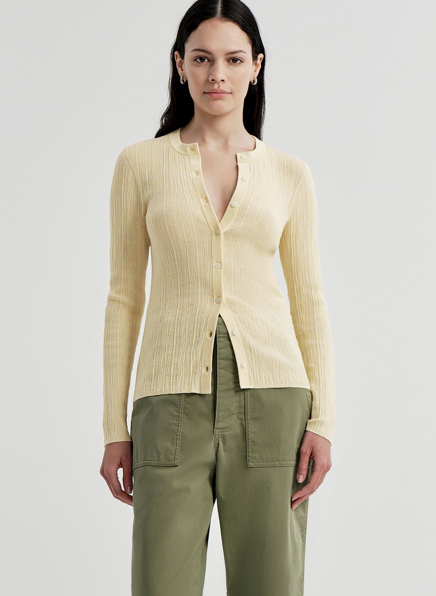 Woman wearing a light-colored ribbed cardigan and green pants on a plain background