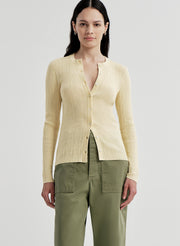 Woman wearing a light-colored ribbed cardigan and green pants on a plain background