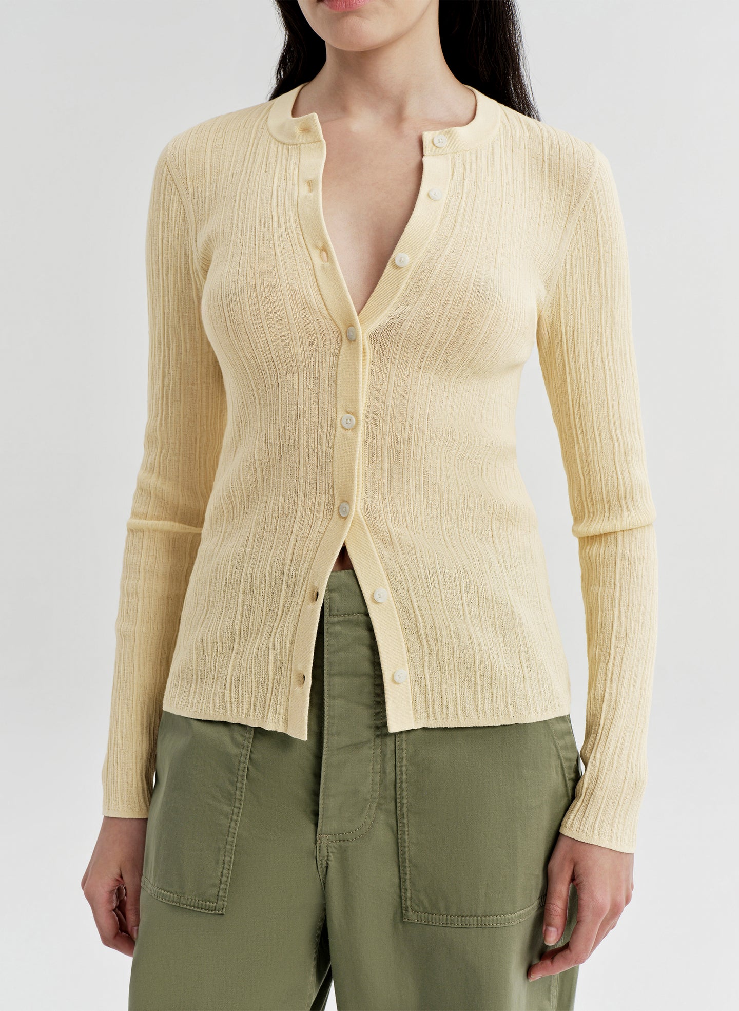 Woman wearing a light yellow ribbed cardigan over a green top on a white background
