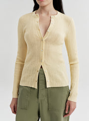 Woman wearing a light yellow ribbed cardigan over a green top on a white background