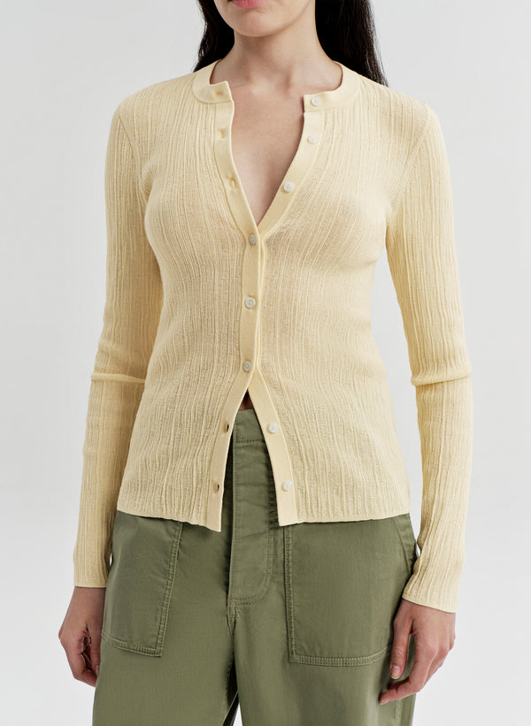 Woman wearing a light yellow ribbed cardigan over a green top on a white background