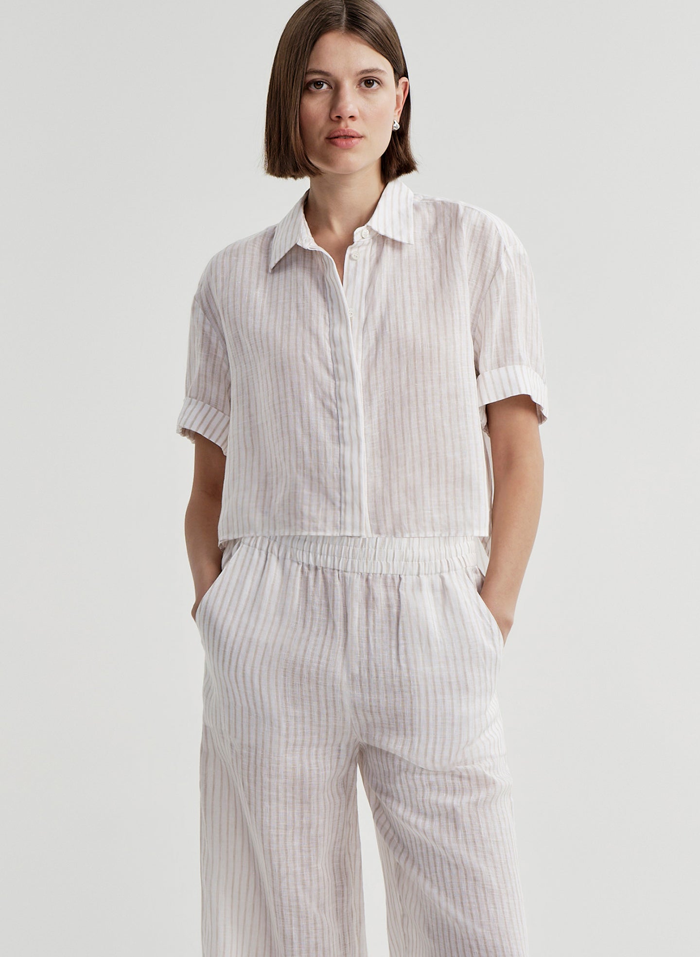 Woman wearing a white striped collared shirt with striped pants on a light gray background