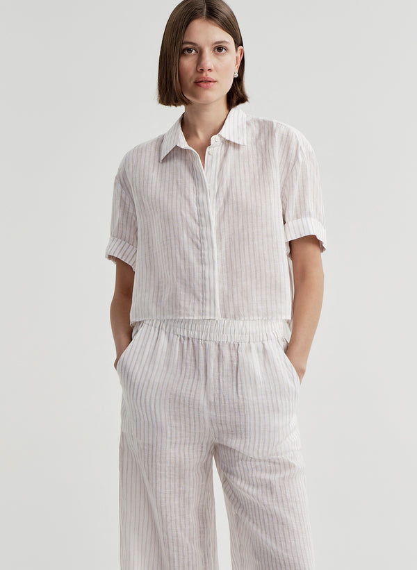 Woman wearing a white striped collared shirt with striped pants on a light gray background