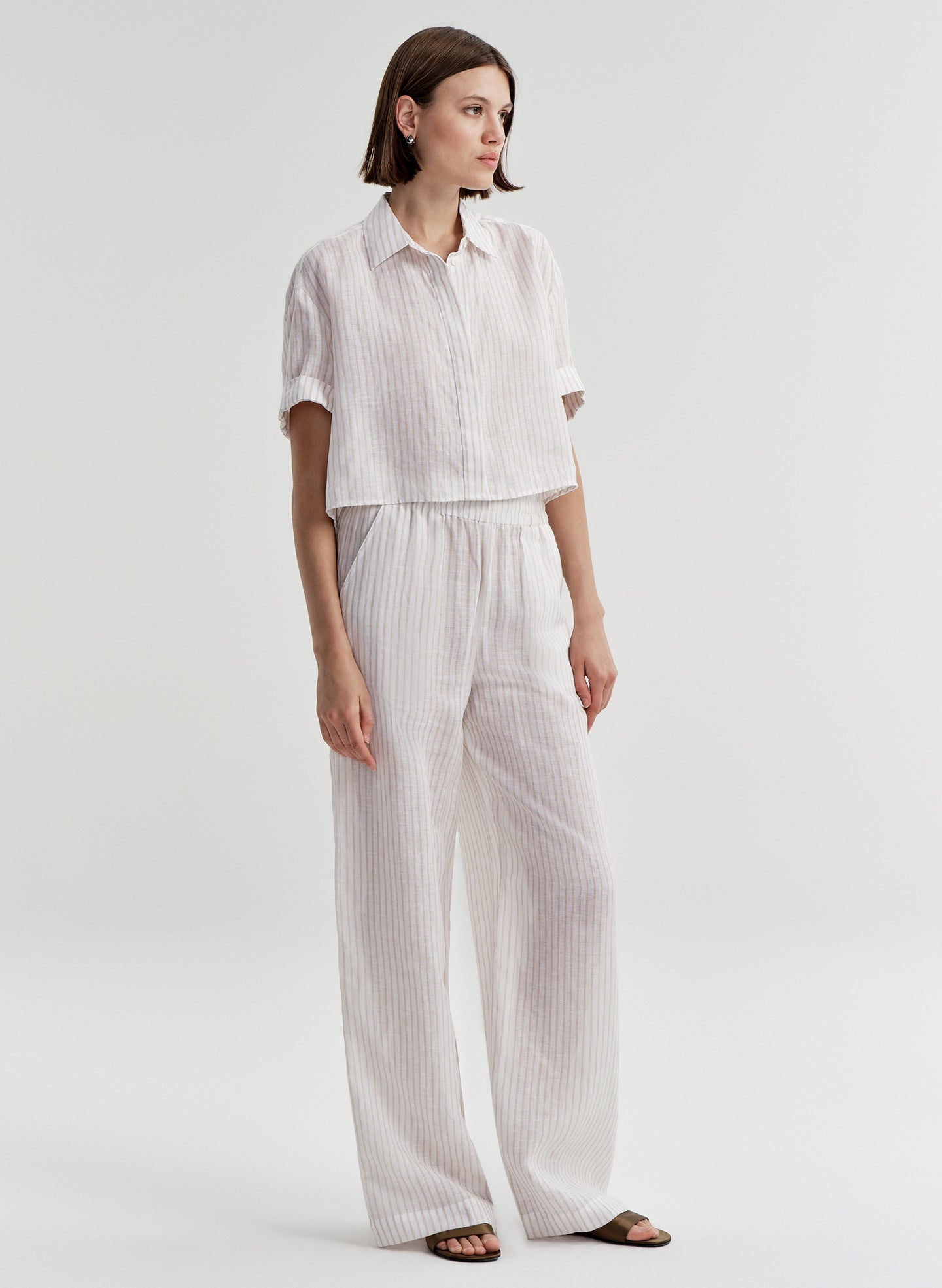 Woman wearing a white striped collared shirt with striped pants on a light gray background