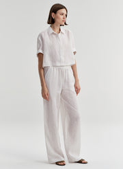 Woman wearing a white striped collared shirt with striped pants on a light gray background
