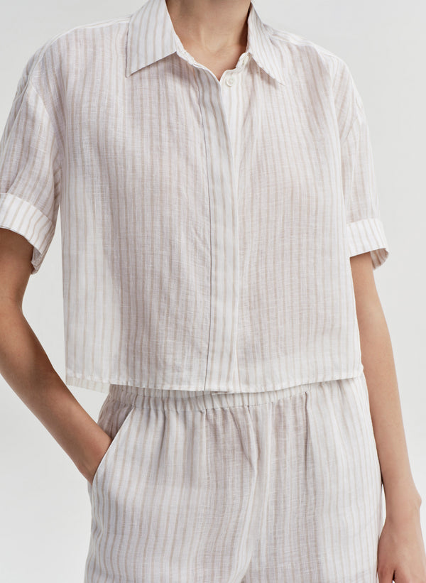 Woman wearing a white striped collared shirt with striped pants on a light gray background