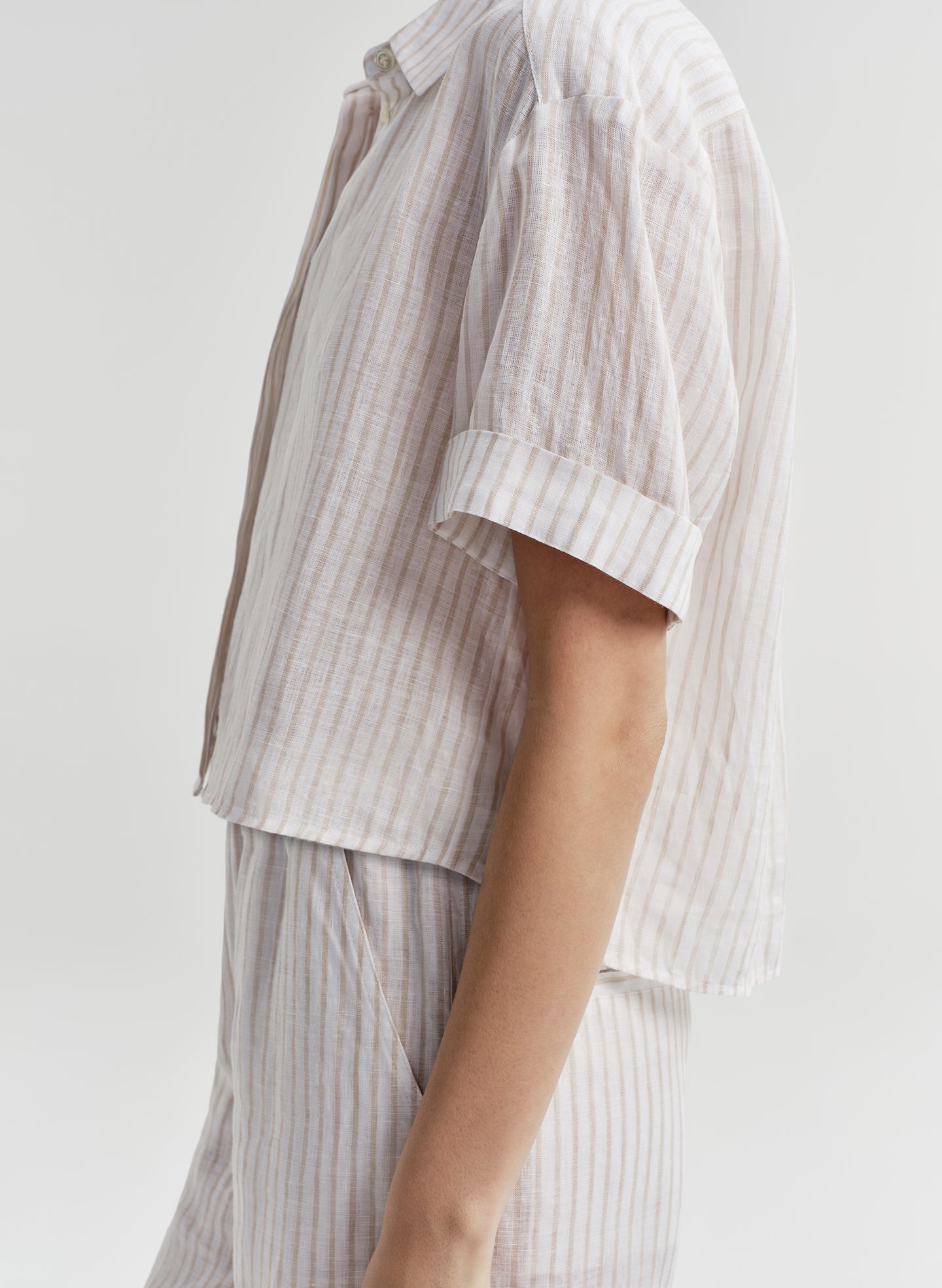 Woman wearing a white striped collared shirt with striped pants on a light gray background