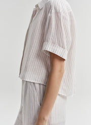 Woman wearing a white striped collared shirt with striped pants on a light gray background