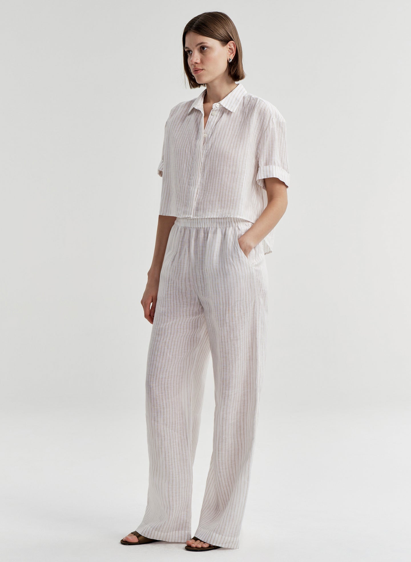Woman wearing striped ivory colored linen wide-leg pants with a matching top on a white background