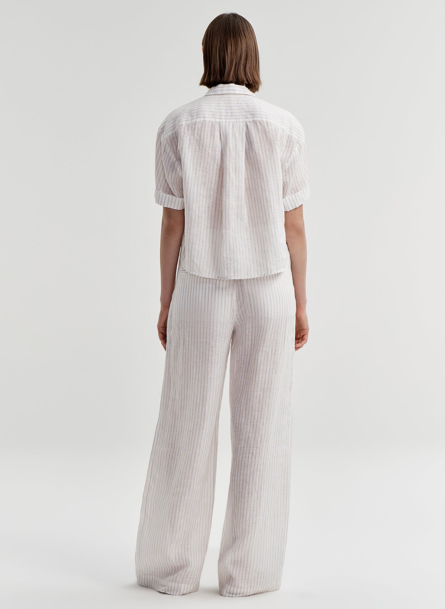 Woman wearing striped ivory colored linen wide-leg pants with a matching top on a white background